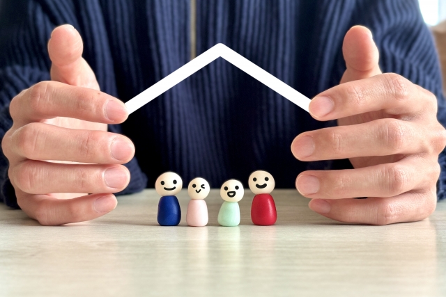 屋根の下で家族の人形が笑っているのを手が守っている様子の画像